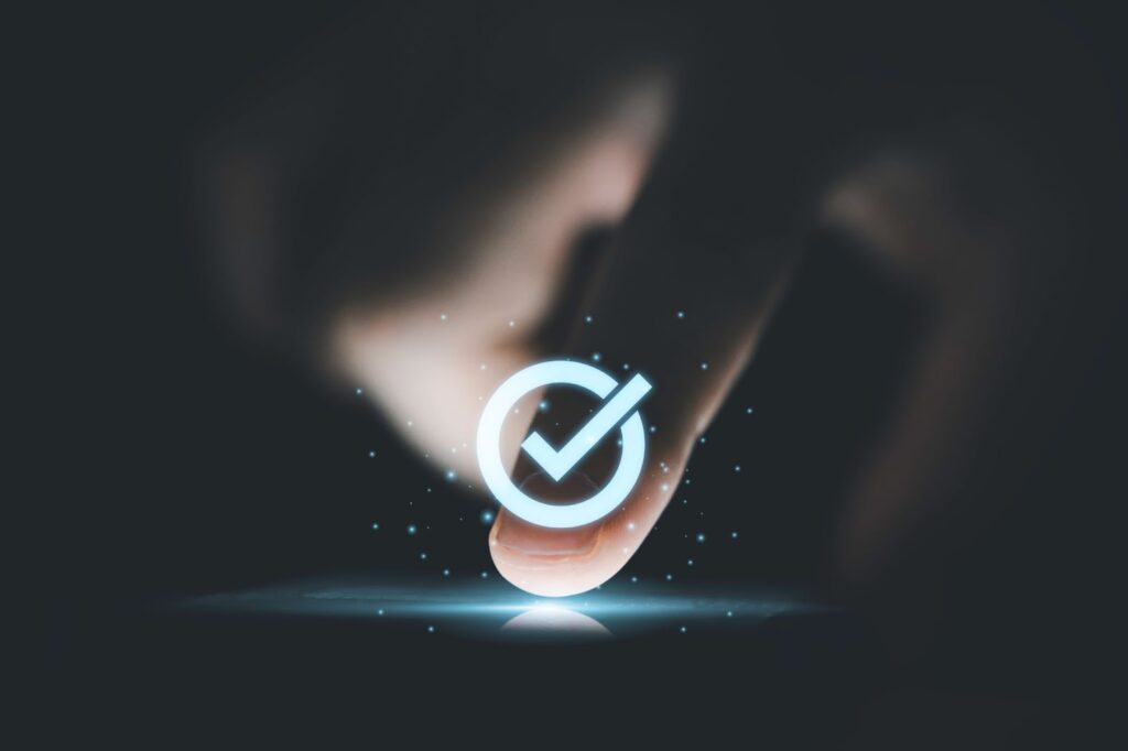 Close-up of a finger touching a digital screen with a glowing checkmark symbol, representing confirmation or successful verification in a digital interface.