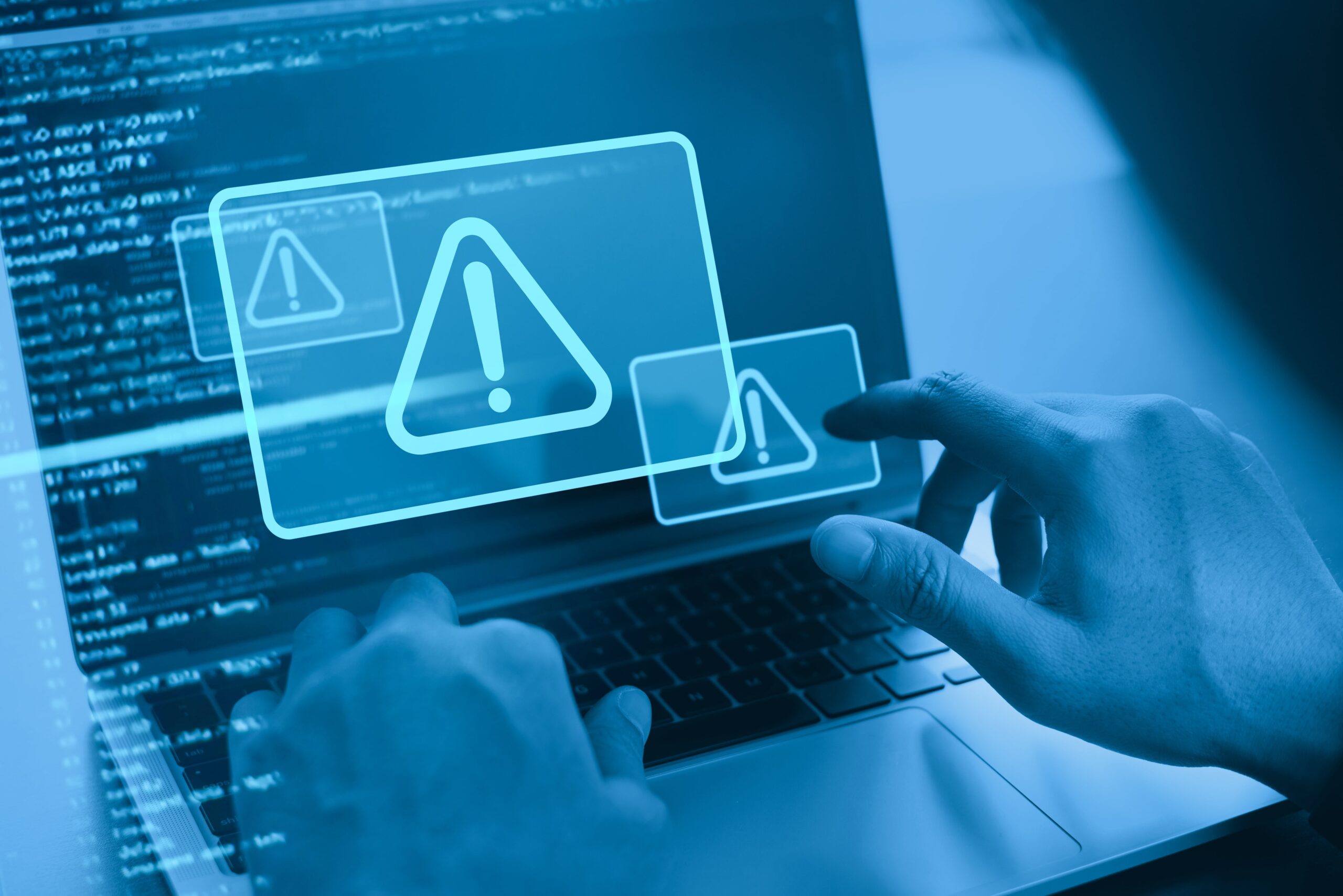 Person interacting with warning icons on a laptop screen, symbolizing cyber threats and data security risks.